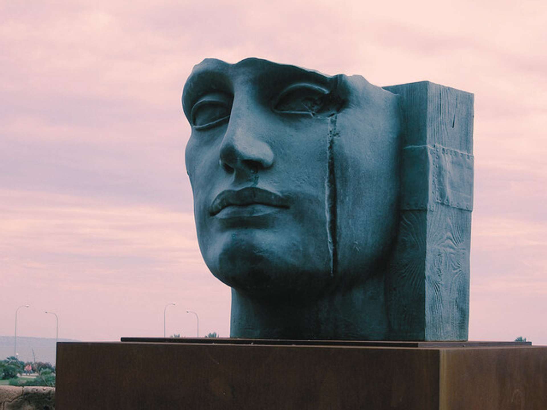 a haunting sculpture of a face with a crack in front of a pink sky